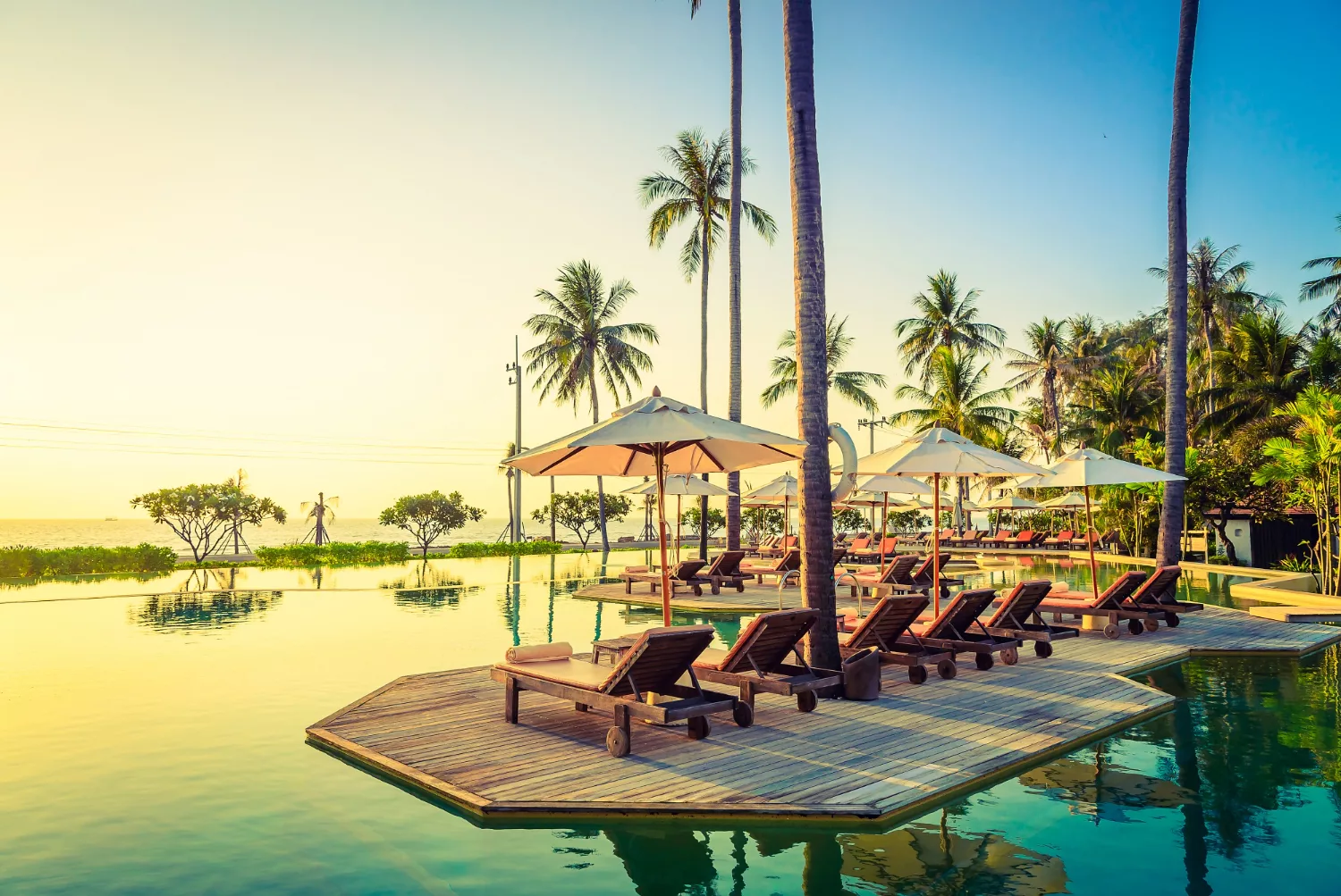 An exclusive, low-density private villa infinity pool overlooking a secluded ocean cove during sunset